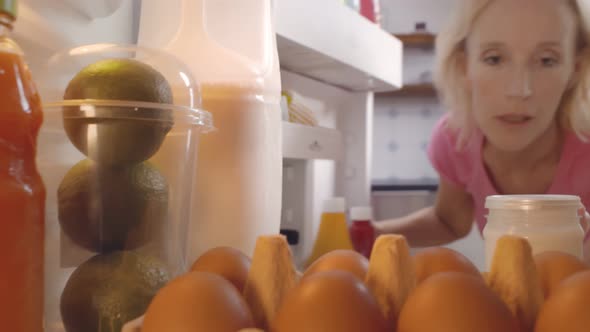 Mature Woman Taking Bottle of Cream Sauce From Fridge alt