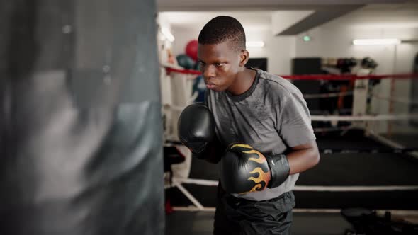 Young Concentrated African Male Boxer Hitting Punching Bag in Boxing Club alt