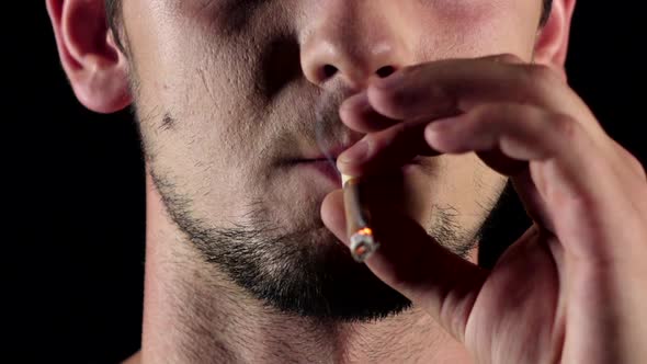 Man Smokes a Cigarette. He Holds a Cigarette Between Two Fingers. Black. Close Up. Slow Motion alt