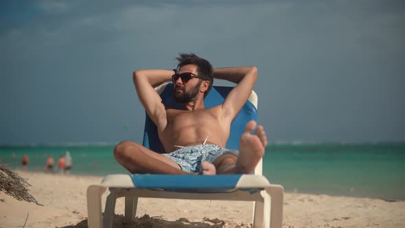 Tan Man Relaxing On Vacation Caribbean Tropical Beach. Summer Sunbathing Resort Sea Or Ocean. alt