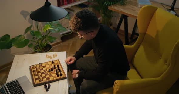Man Plays Chess Online Using Laptop and Chessboard at Home During Lockdown