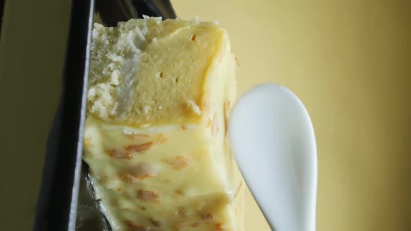 Yellow Glazed Cake with Mango Flavor on a Black Background Picks Up a Spoon alt