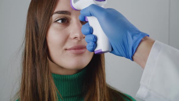 Male Doctor's Hand in Medical Gloves Holding a Noncontact Infrared Thermometer Over the Forehead of alt