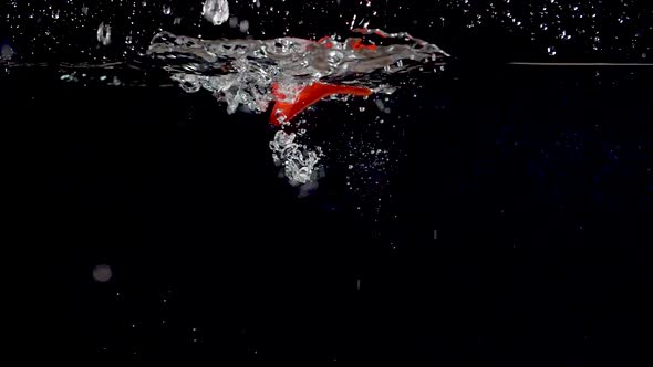 Vibrant red sweet pepper being dropped into water in slow motion. alt