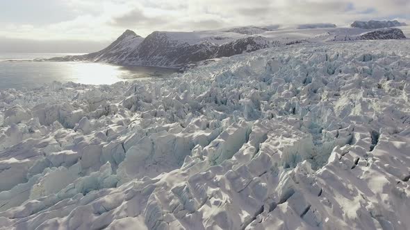 Large glacier reflecting off sunny day in winter, close up drone shot alt