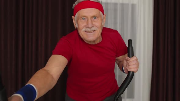 Healthy Elderly Senior Grandfather Model Exercising Sport Workout on Orbitrek in Room at Home alt