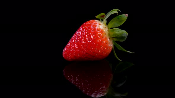 Perfect strawberry rotating on a black polished surface, close up view