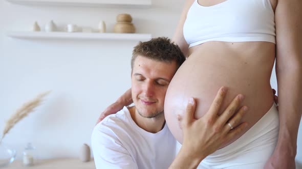 Young Future Father Embracing And Kissing Belly Of His Pregnant Wife alt