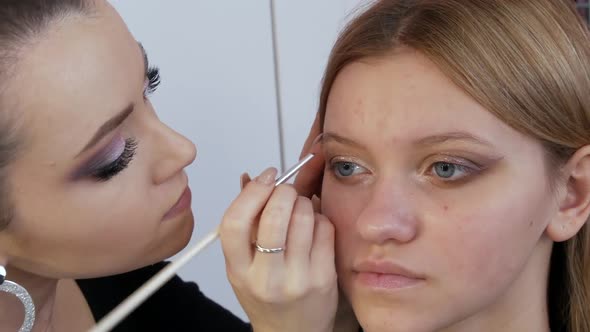 A Professional Makeup Artist Applies a Special Brush with Eyeliner in Beige Color to the Eyes of a alt