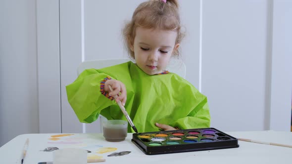 A Young Artist of Two or Three Years Draws Color Circles in Watercolor on White Paper. alt