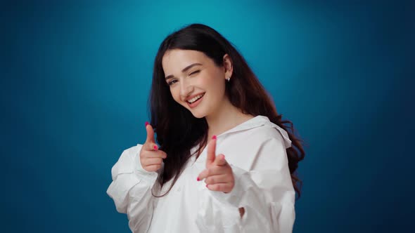 Friendly Smiling Young Woman Pointing to Camera Against Blue Background