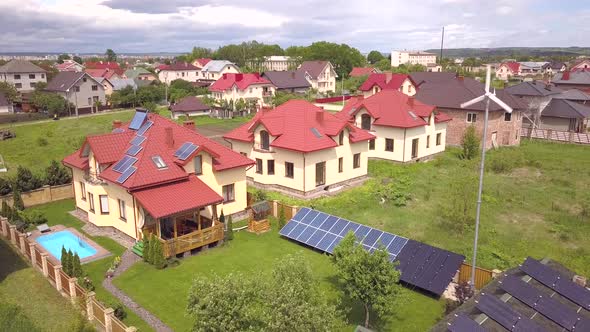 Aerial View of a Residential Private House with Solar Panels on Roof and Wind Generator Turbine alt