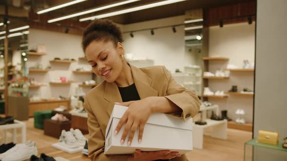 A Happy AfricanAmerican Woman Closes a Box with Her New Shoes in a Luxury Store alt