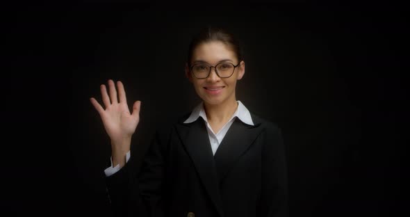 Smiling Asian Woman in Business Clothes Waves Her Hand