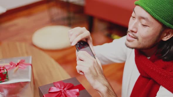 Asian men taking a photo gift box on smartphone decorate Christmas tree celebrates the new year.