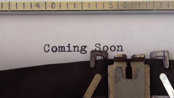 Typing phrase Coming Soon on retro typewriter. Close up. alt