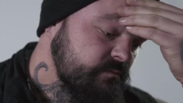Aggressive Bearded Man Rubbing His Forehead To Hold Back Emotions. The Brutal Guy with Tattoos on alt