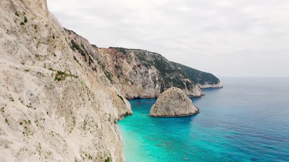 Drone shot of coastline with tall cliff and turquoise sea water. alt
