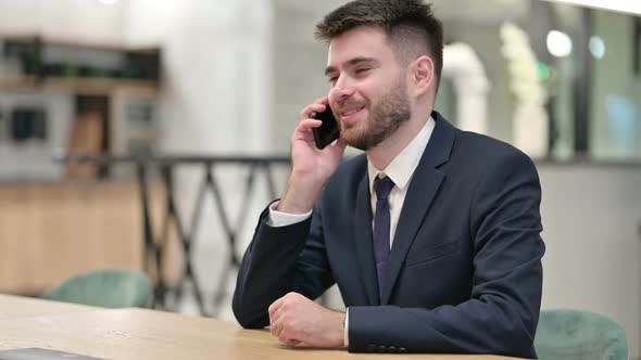 Cheerful Young Businessman Talking on Smartphone in Office alt