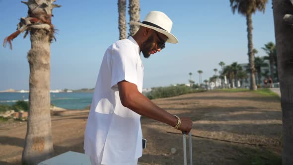 Young Confident African American Male Tourist Walking with Trolley Bag in Slow Motion Sitting Down alt