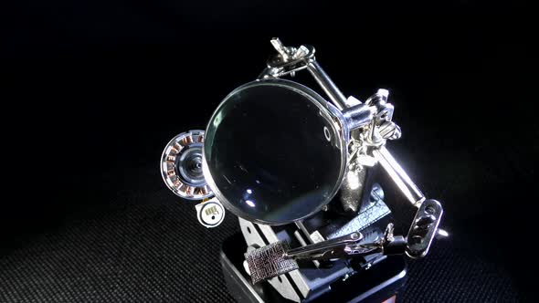 Stepper motor stator in clip holder with magnifying glass.