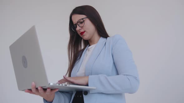 Spectacular Young Business Lady Working on a Laptop While Standing on a White Background alt