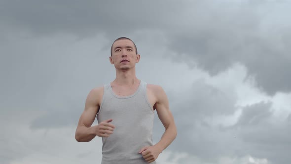 Man of Asian Appearance Runs with Concentration Against Background of Thunderstorms Sky Front View alt