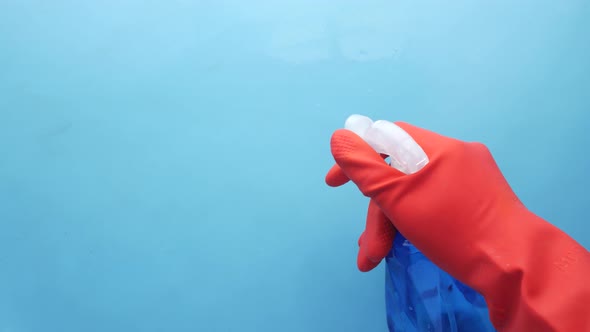Hand in Blue Rubber Gloves Holding Spray Bottle with Copy Space alt