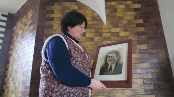 Senior 60s Woman Speak with Old Photo Portrait of an Ancestor