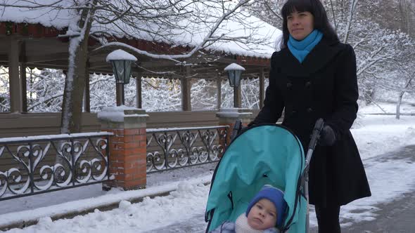 Mother Walks In Park With Her Child In Stroller. Snowy Winter 5 alt