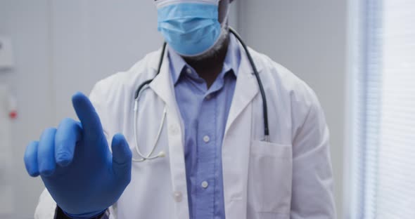 Midsection of african american male doctor wearing face mask and surgical gloves alt
