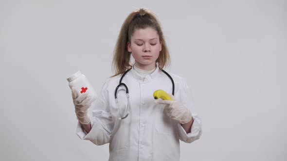 Caucasian Little Doctor Choosing Between Pills and Banana Stretching Fruit to Camera Shaking Head alt