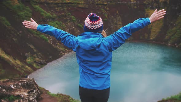 Young Tourist Woman in Jacket and Hat Rise Her Hands Enjoying Beautiful View of Kerid Lake of alt