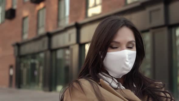 Nice Girl Brunette White Virus Mask on Her Face Sitting on Bench alt