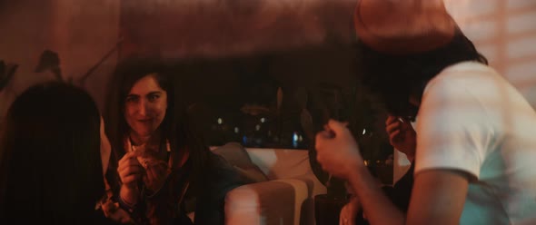 Group of young friends having fun and eating pizza in moody lights alt