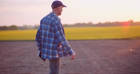 Agriculture - Farmer Walking on Field Examining Crops at Farm at Dusk alt