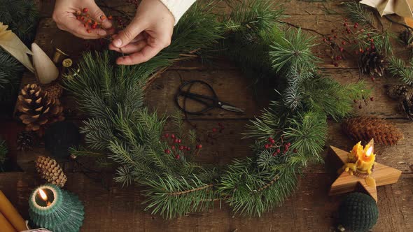 Making Christmas wreath on rustic wooden table with candle, decorations, cones