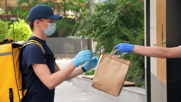Delivery Man Wears Protective Medical Face Mask and Gloves Picks Up Paper Bag alt