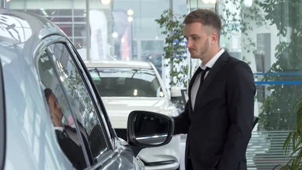 Young Businessman in a Suit Examining Cars for Sale at the Dealership alt