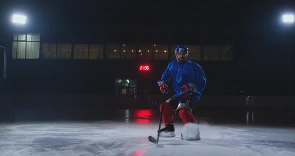 Man Hockey Player in Hockey Uniform Leaves with a Stick in His Hands Out of the Darkness and Looks alt