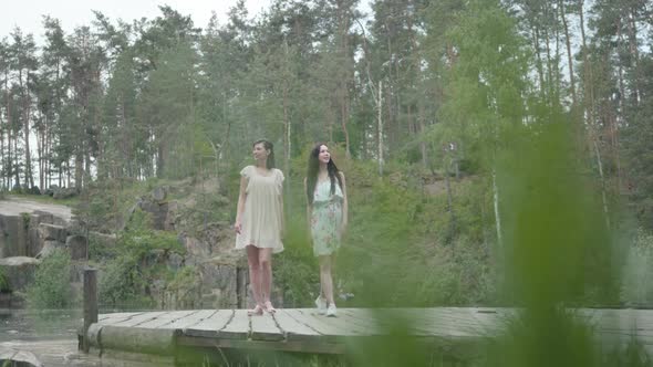 Two Adorable Women Wear Summer Dresses Standing in the Top of Rock and Looking at Amazing View alt
