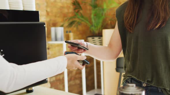 Caucasian waitress receiving contactless payment and giving coffee cup to caucasian female customer alt