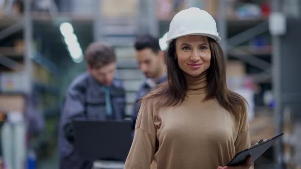 Gorgeous Caucasian Woman Standing in Warehouse with Paperwork Smiling Looking at Camera alt