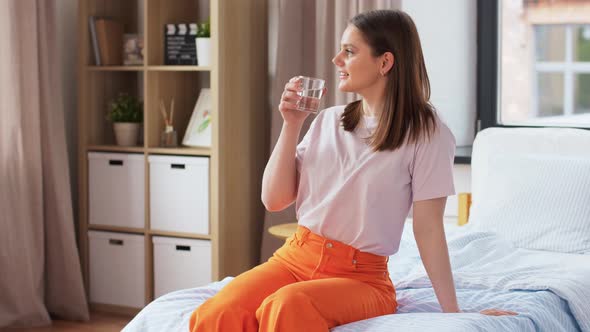 Girl with Glass of Water Sitting on Bed at Home