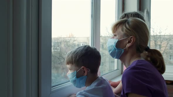 Mother, son and daughter in medical masks near the window in isolation for virus outbreak .