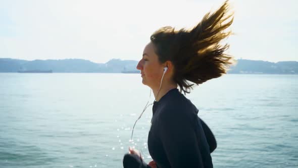 Smiling Young Woman Running at Riverside alt