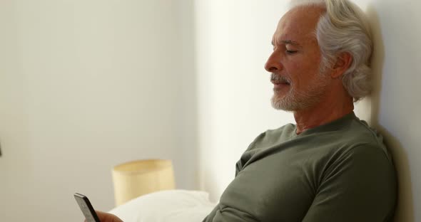 Senior man using mobile phone in bedroom at home 4k alt
