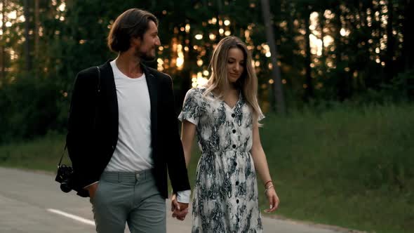 Young European Couple on a Date Is Talking and Walking Past Nature Down a Sidewalk alt