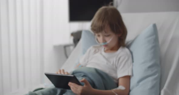 Preteen Kid Patient Lying in Hospital Bed Using Tablet with Dropper in Hand alt