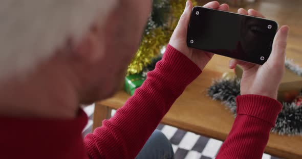 Happy albino african american man wearing santa hat using smartphone at christmas alt